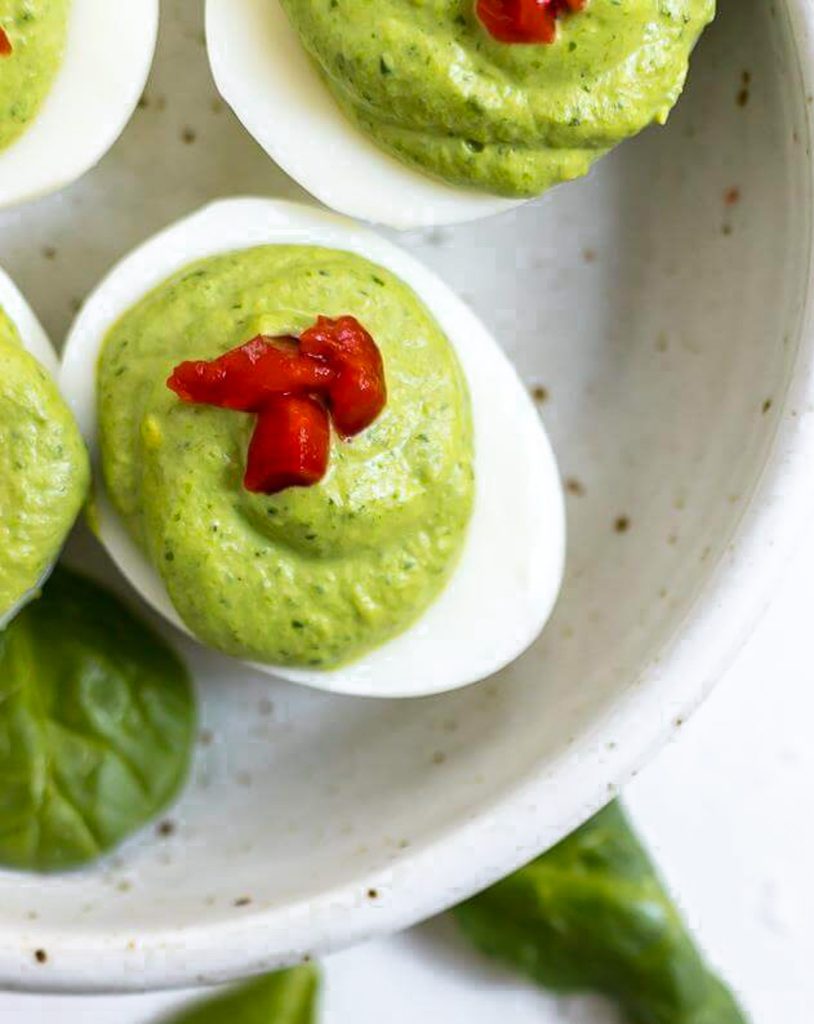 deviled egg with green filling topped with pimentos